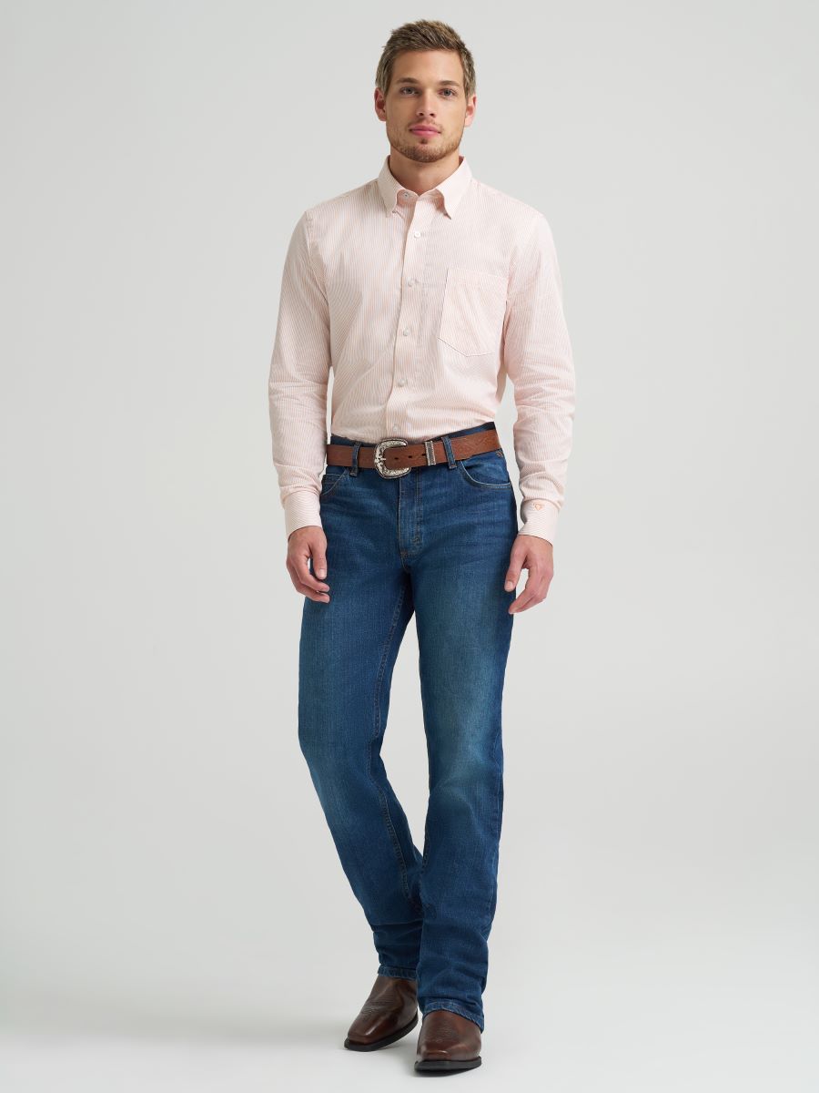 Man wearing a light pink Wrangler shirt and blue jeans on a plain background