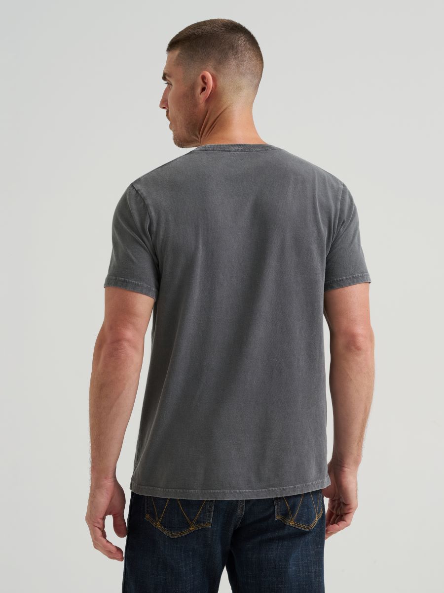 Man wearing a black Wrangler t-shirt and dark jeans against a plain background