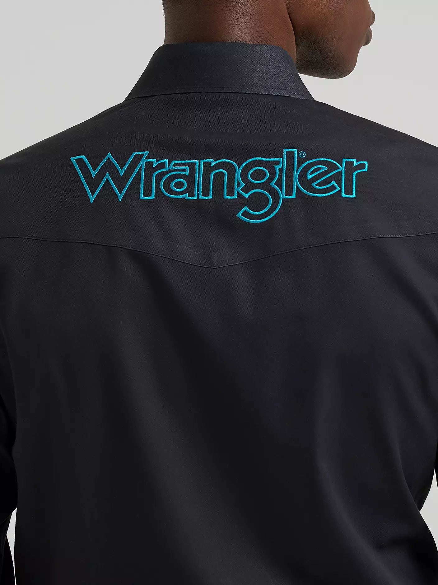 Person wearing a black Wrangler shirt with branding on a gray background