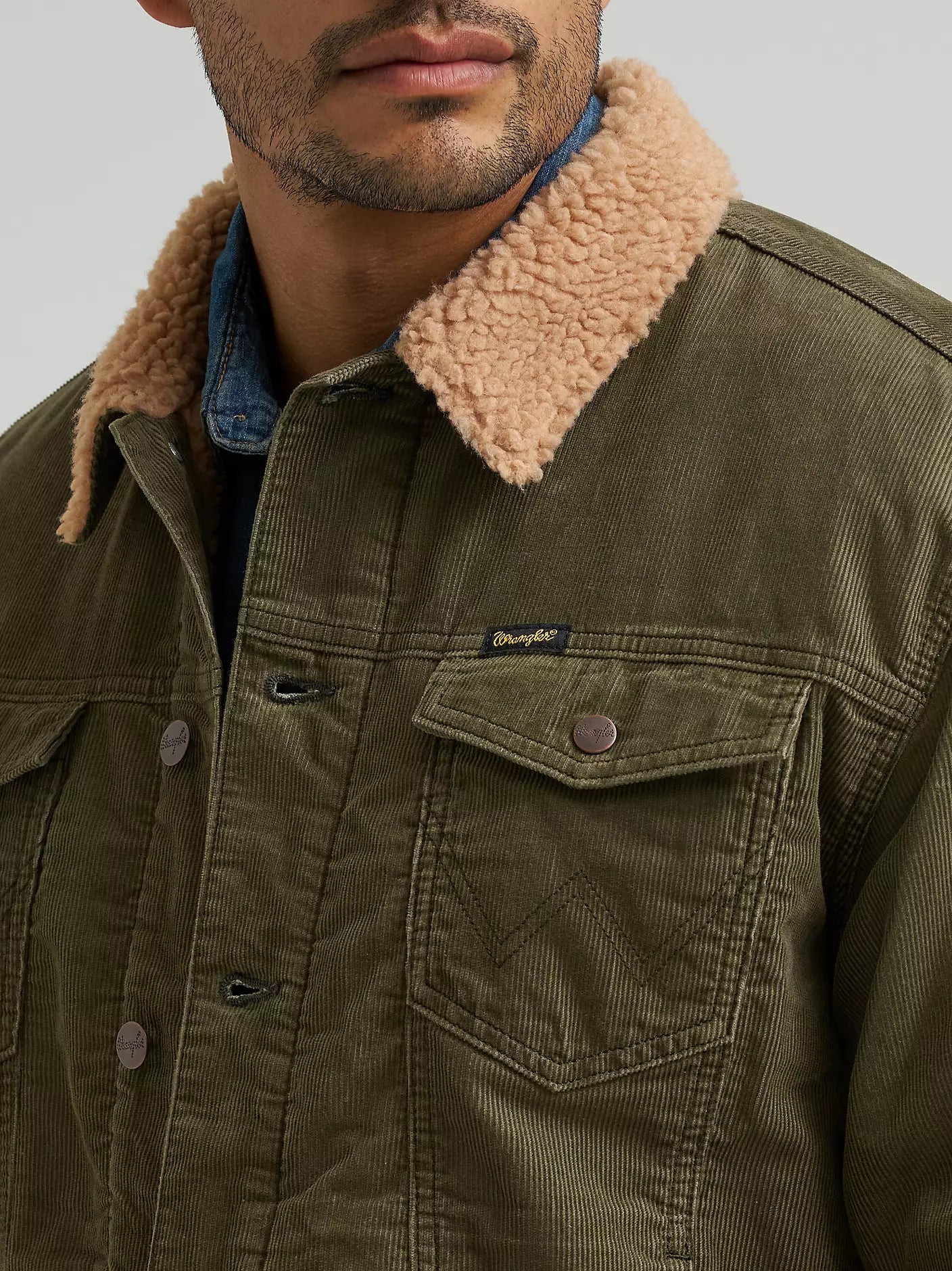 Close-up of a man wearing a Wrangler corduroy jacket with a tan sherpa fleece collar, layered over a blue denim shirt. The Wrangler logo is visible on the chest pocket.