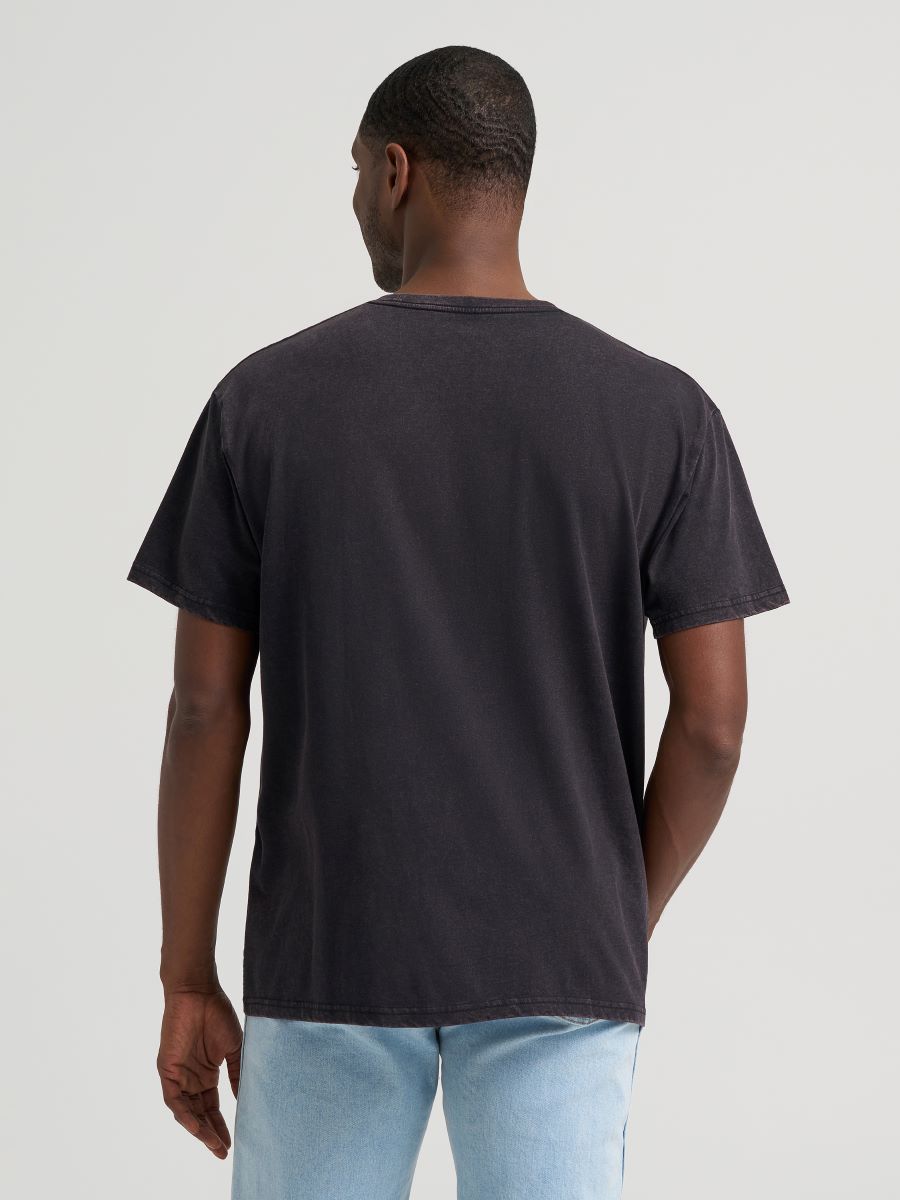 Man wearing a black Wrangler tshirt and blue jeans on a grey background