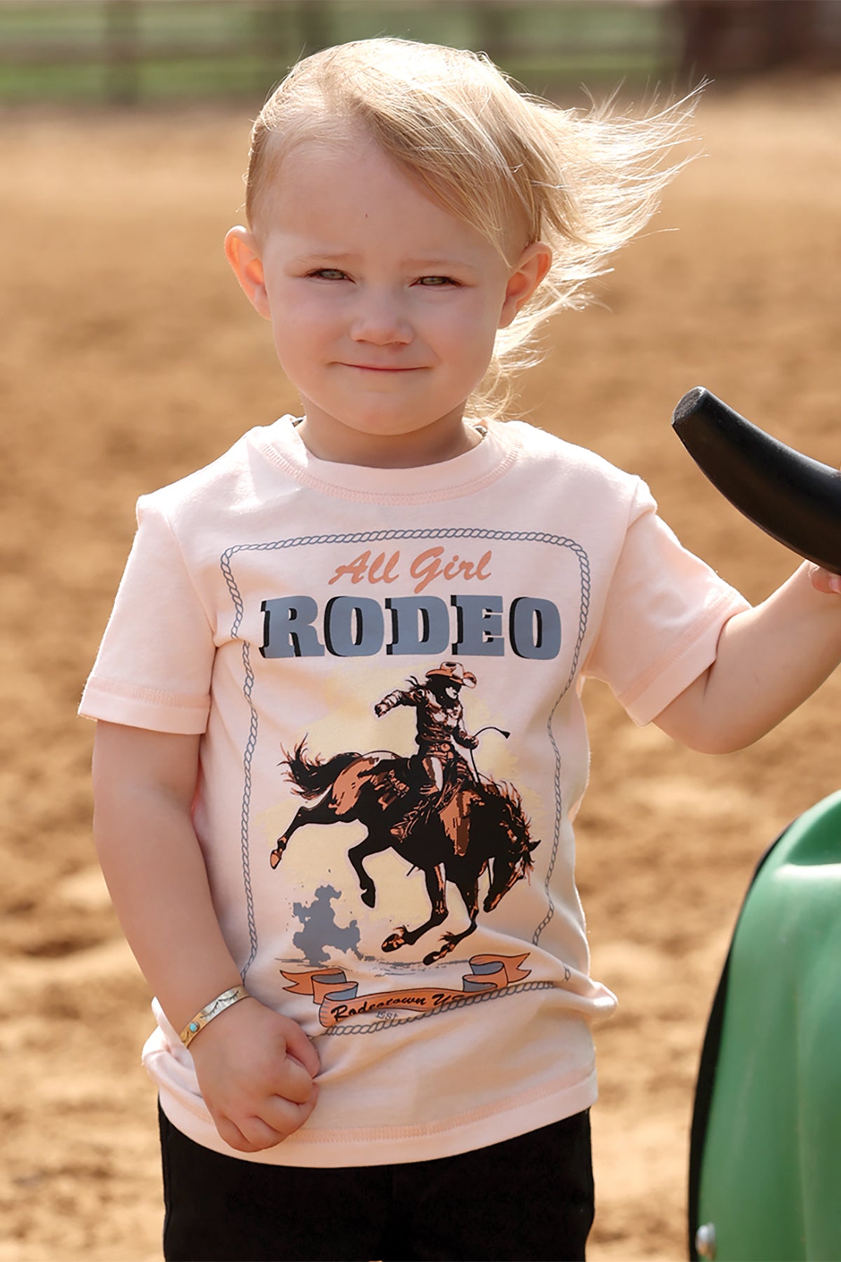 Child wearing a 'All Girl Rodeo' t-shirt by cruel girl with a cowboy graphic in an outdoor setting.
