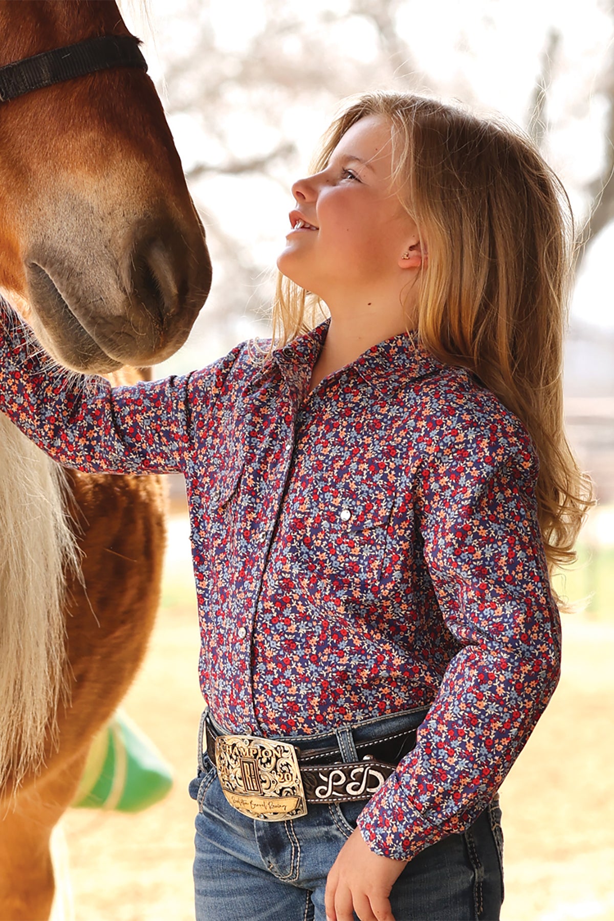 Girl in a floral shirt by cruel girl standing next to a horse outdoors