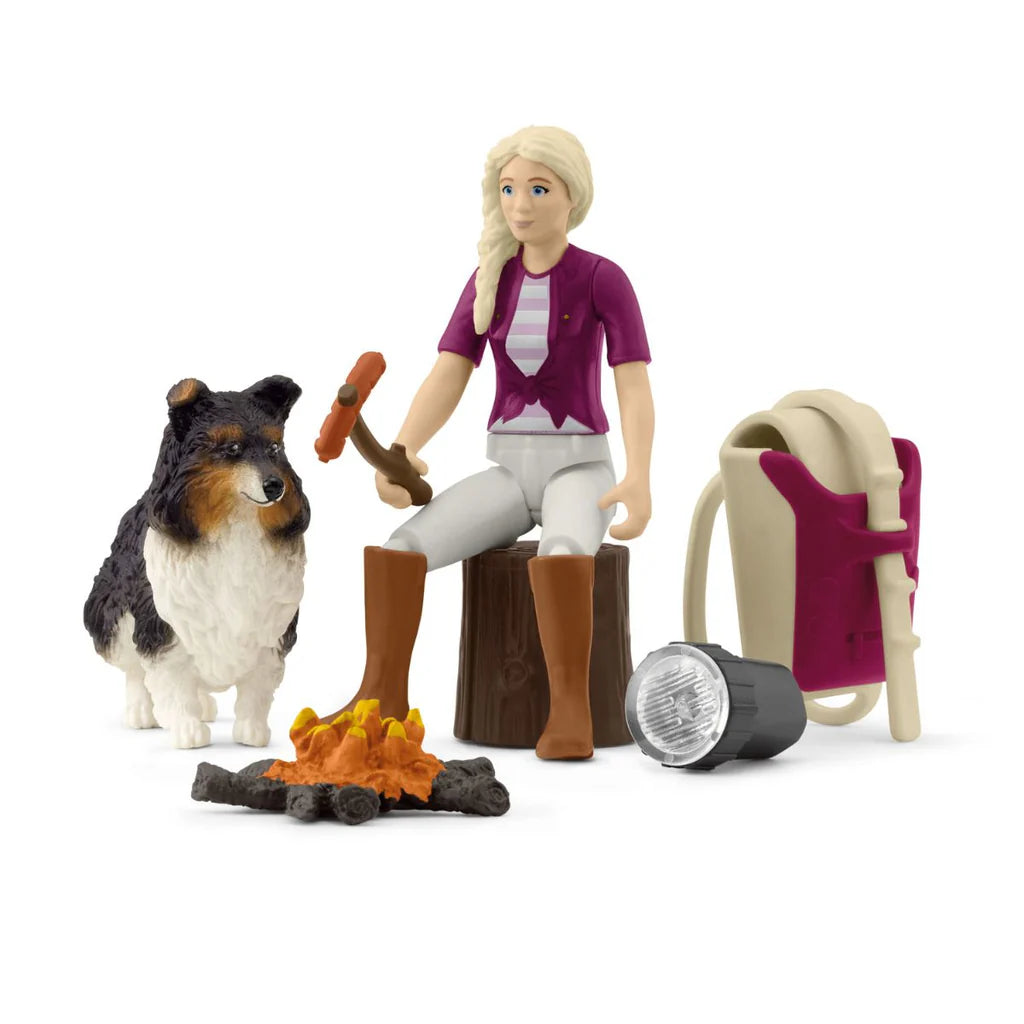 Schleich toy figurine of a person with a dog by a campfire, surrounded by camping gear on a white background
