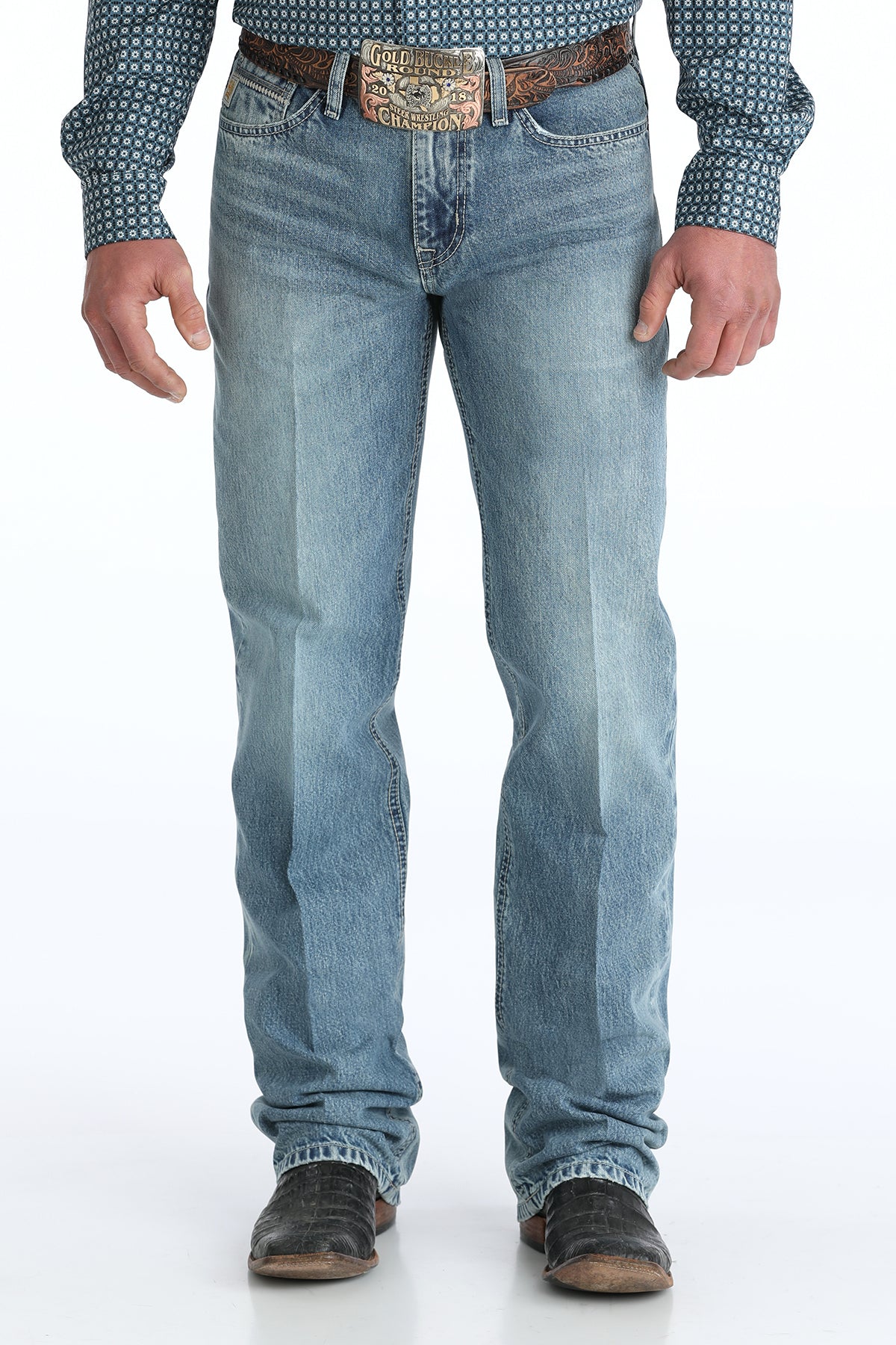 Person wearing relaxed light blue Cinch jeans with a patterned shirt and brown belt on a white background