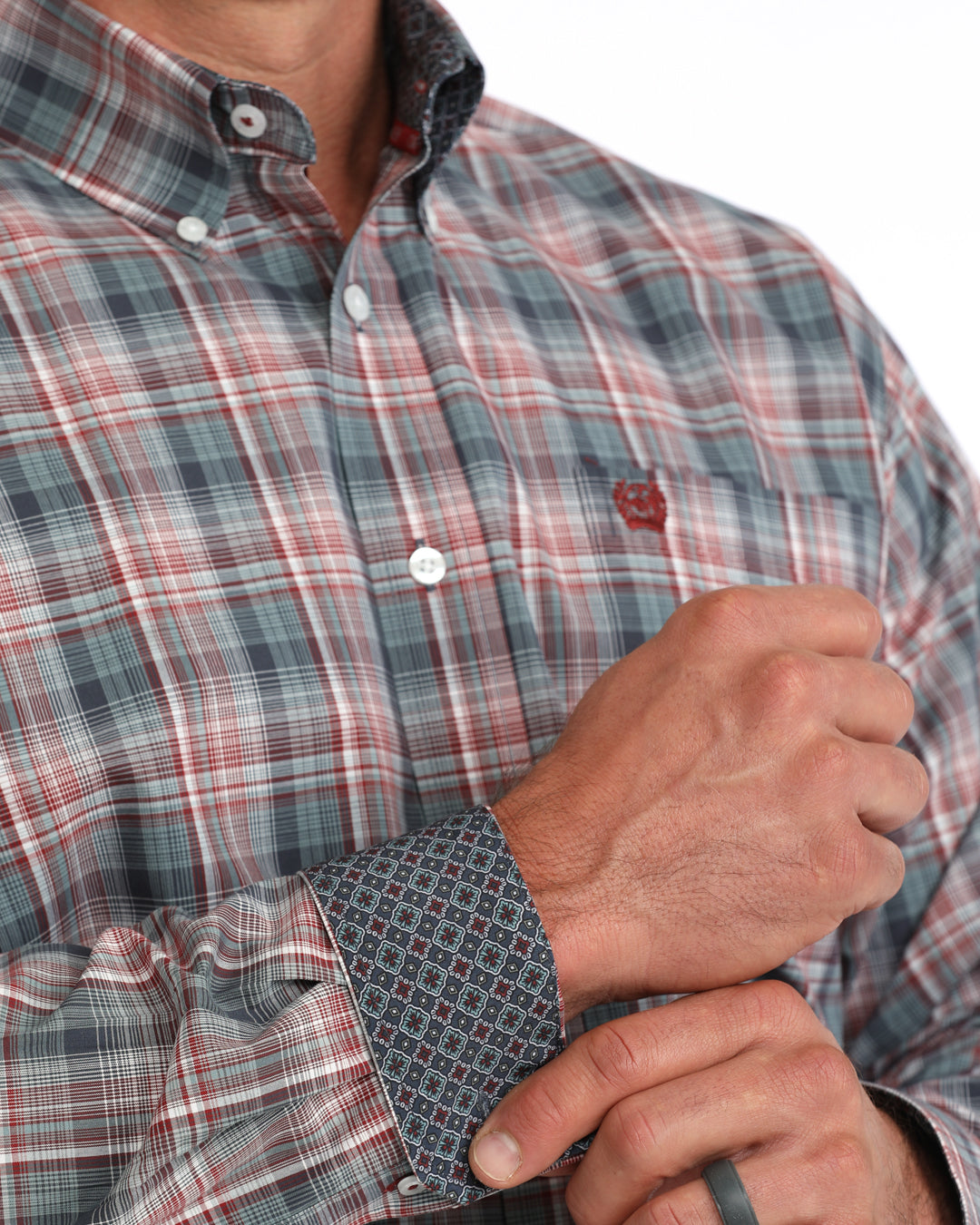 A close-up of a man wearing a long-sleeve plaid button-down Cinch shirt in muted red, gray, and blue tones, with his hands adjusting the patterned cuff.
