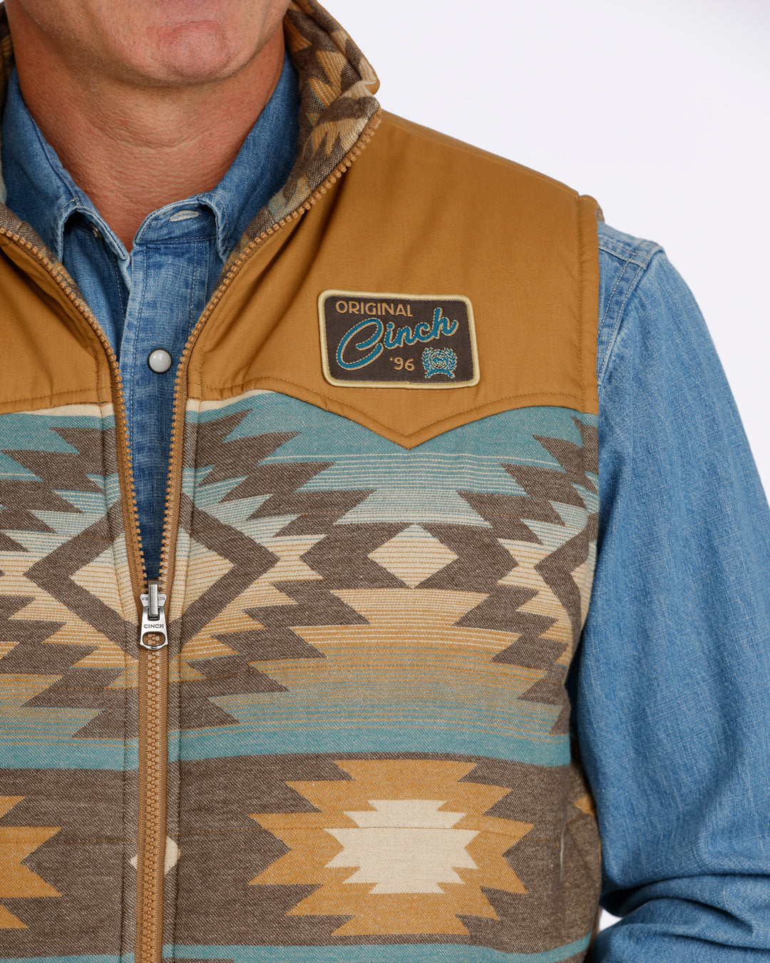 man wearing a tan Cinch vest with bue aztec design and a denim shirt on a white background