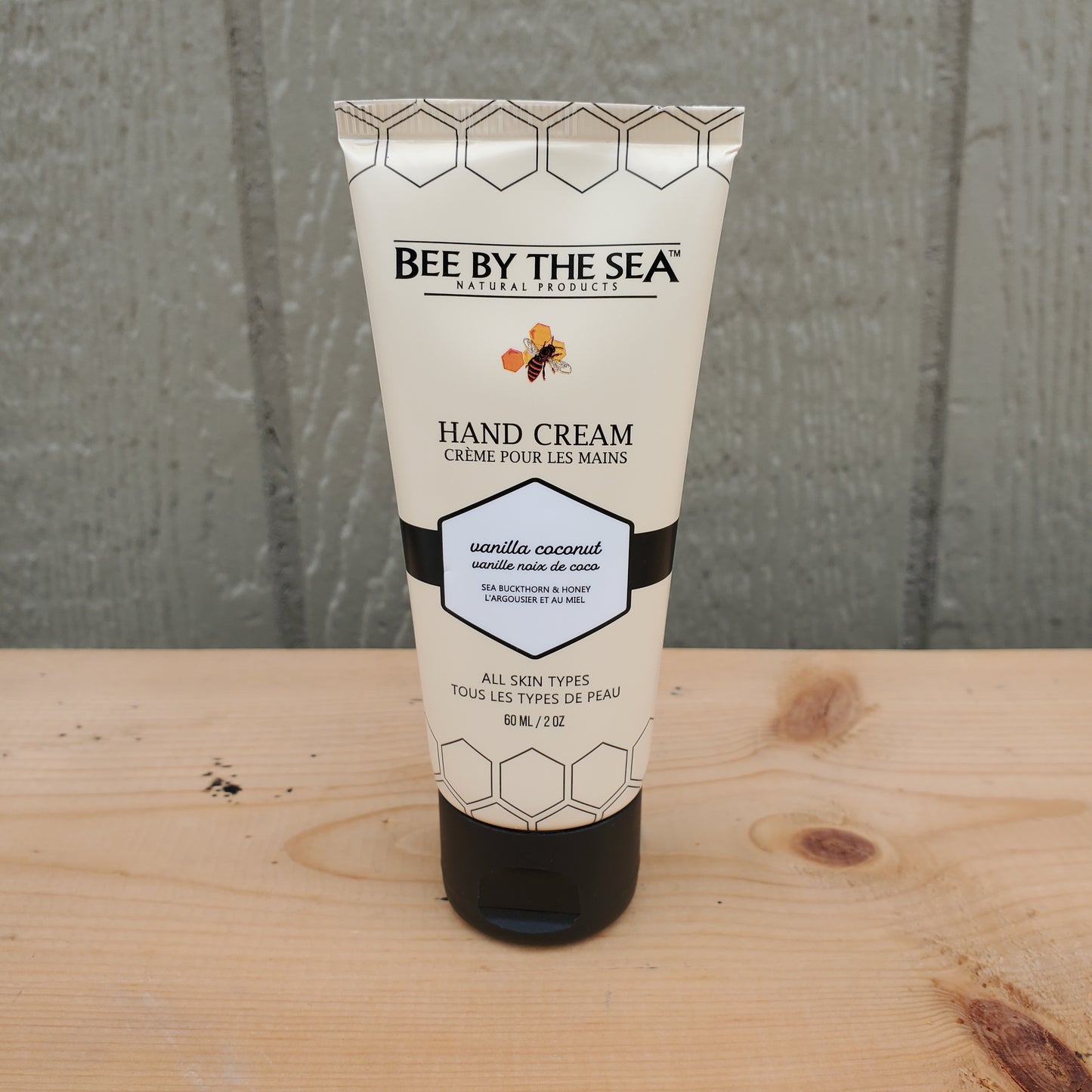 Hand cream tube labeled 'Bee by the Sea' on a wooden surface.