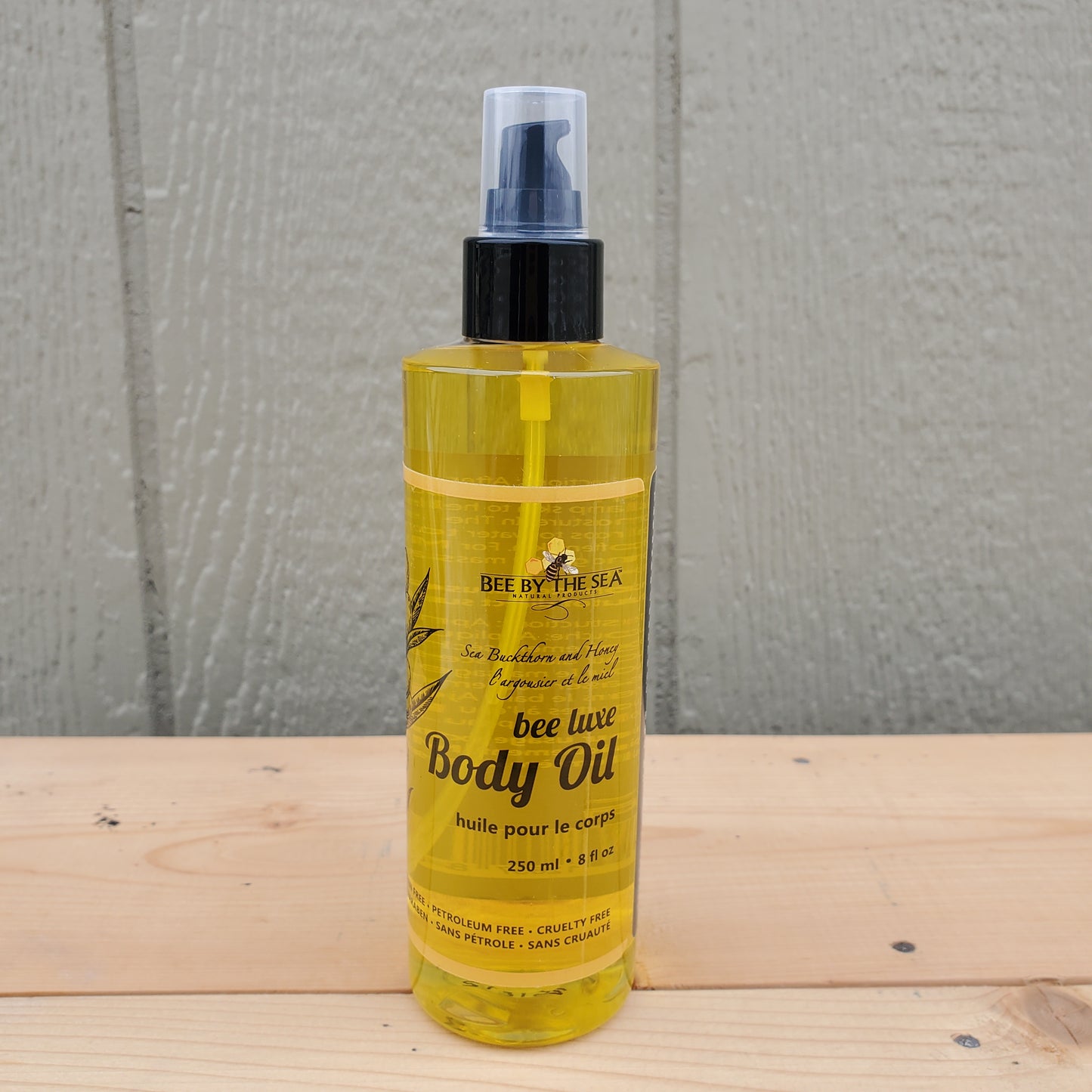Bee by the sea body oil spray bottle on a wooden surface with a green background