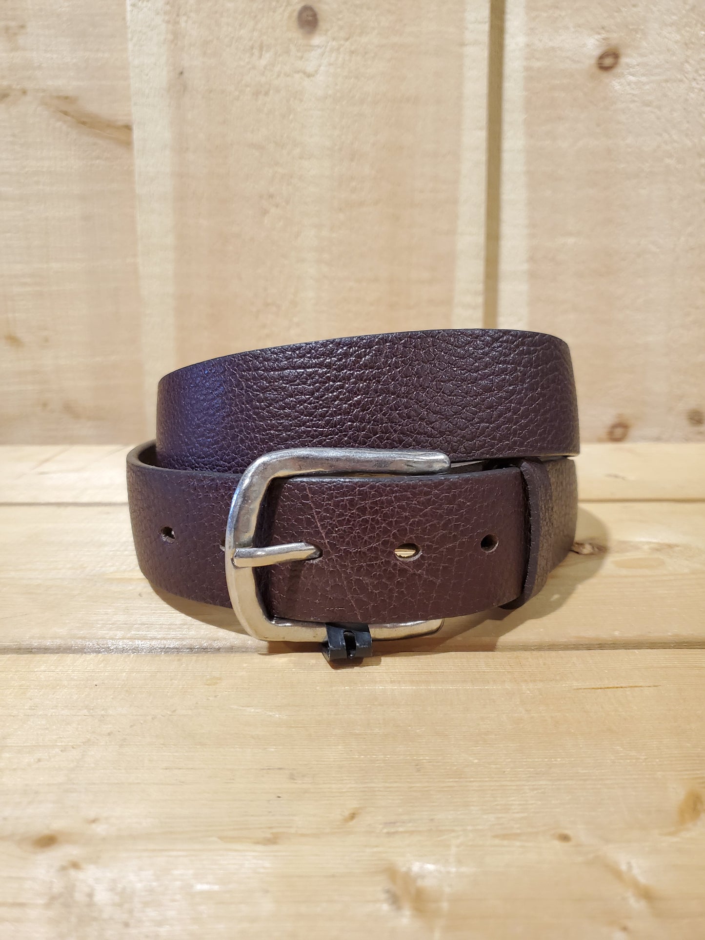 A brown leather men's belt with a buckle, displayed on a wooden background.