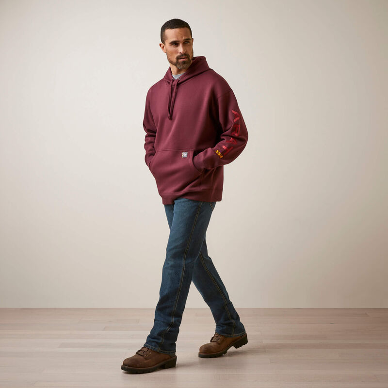 Man wearing a maroon Ariat hoodie with a brand logo, blue jeans, and brown shoes on a plain background