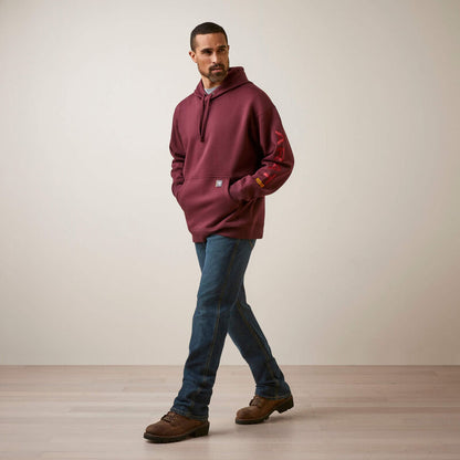 Man wearing a maroon Ariat hoodie with a brand logo, blue jeans, and brown shoes on a plain background