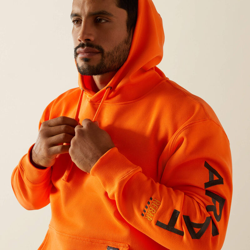 Man wearing an orange Ariat hoodie with text on sleeves against a plain background