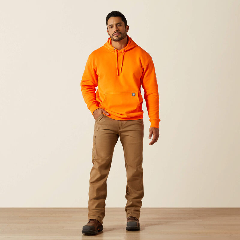 Man wearing an orange Ariat hoodie and brown pants standing against a plain background