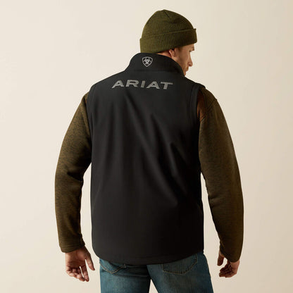 Man wearing a black Ariat vest, brown sweater, blue jeans and a green toque on a cream colored background