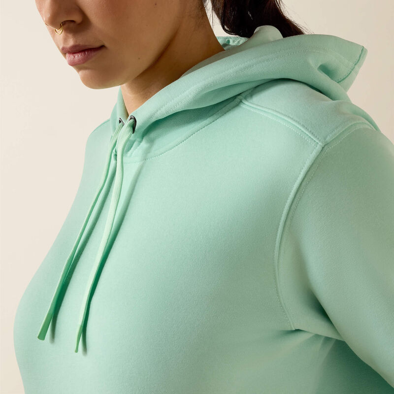 Person wearing a light green Ariat hoodie on a beige background