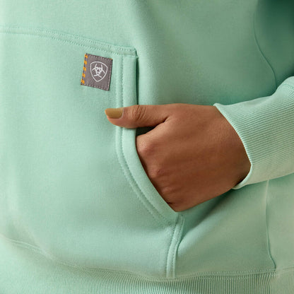 Light green Ariat sweatshirt with a brand logo on the chest pocket, worn by a person.