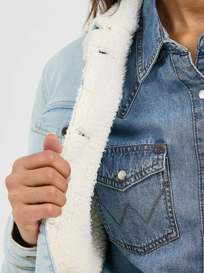 Woman wearing a light denim Wrangler sherpa lined jacket, and a denim shirt on a white background
