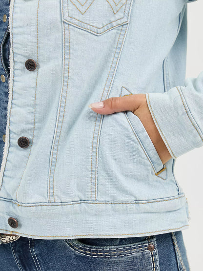 Woman wearing a light denim Wrangler sherpa lined jacket and blue jeans on a white background