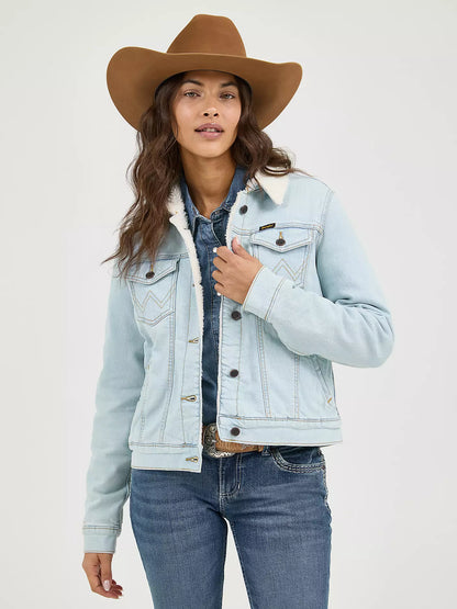 Woman wearing a light denim Wrangler sherpa lined jacket, blue jeans and a brown cowboy hat on a white background