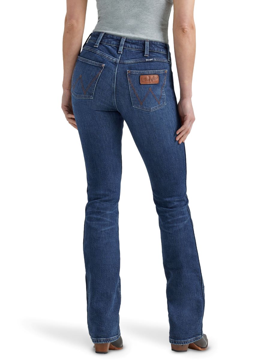 A woman standing and facing away from the camera, wearing retro dark wash high rise boot cut jeans with a leather patch on the back pocket.