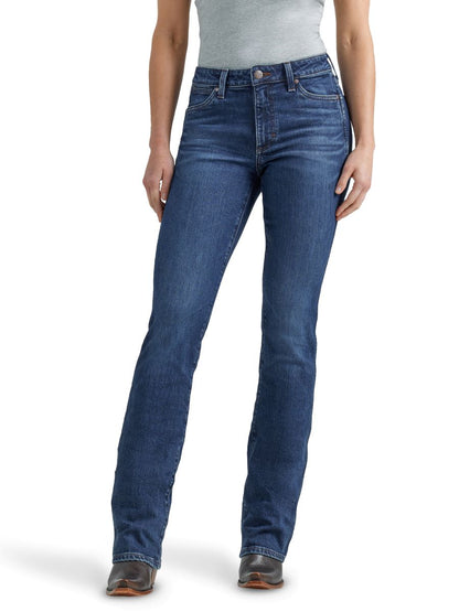 A woman standing and facing toward the camera, wearing retro dark wash high rise boot cut jeans with a leather patch on the back pocket.