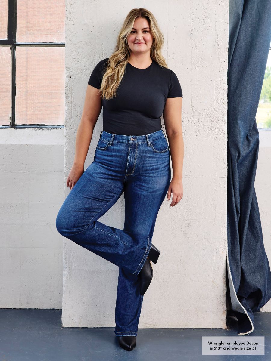 Woman wearing blue jeans and a black top against a white wall.