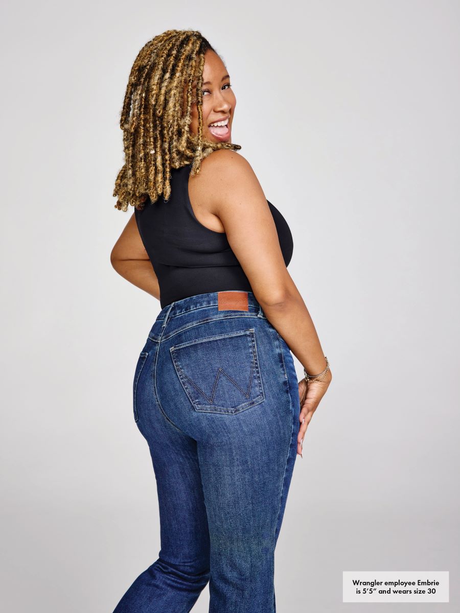 Woman wearing blue jeans and a black top on a plain background
