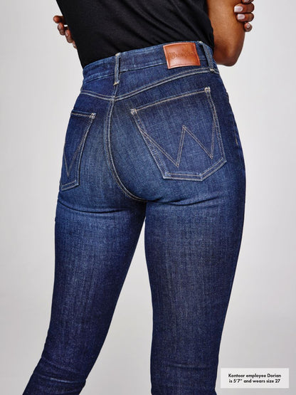 Person wearing blue jeans with a visible brand logo on a light gray background