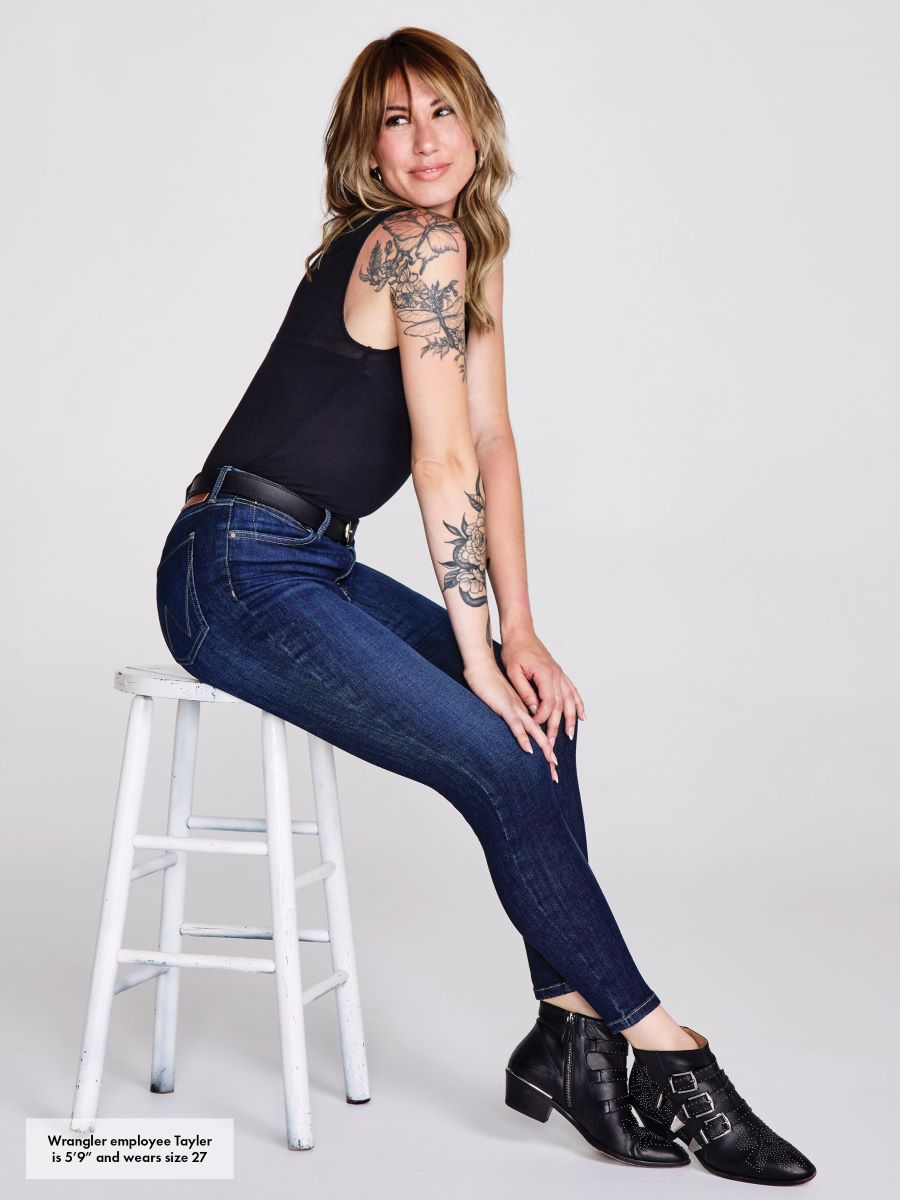 Woman sitting on a stool wearing blue jeans and black shoes against a white background