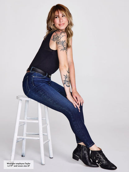 Woman sitting on a stool wearing blue jeans and black shoes against a white background
