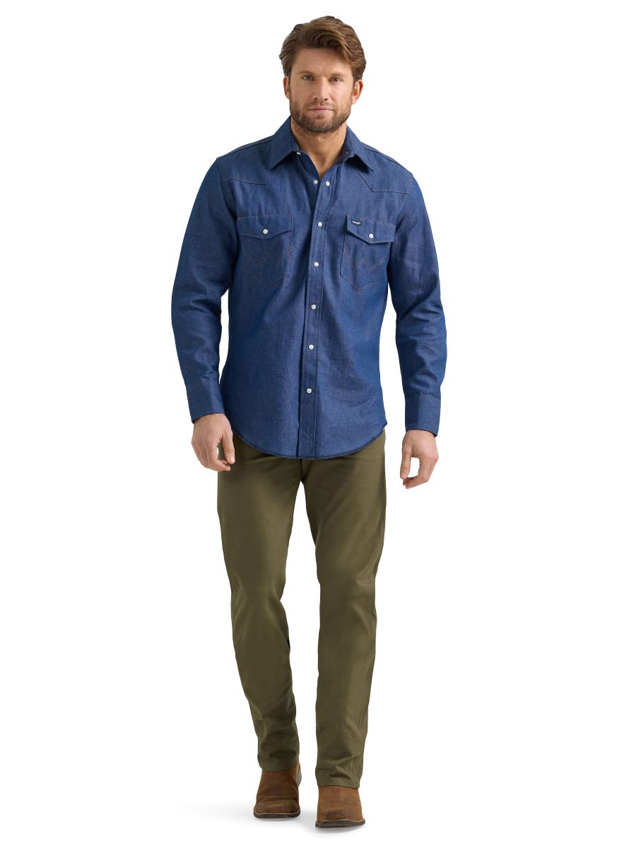 A man wearing a pair of olive green Wrangler cowboy cut canvas jeans, denim shirt and brown boots.