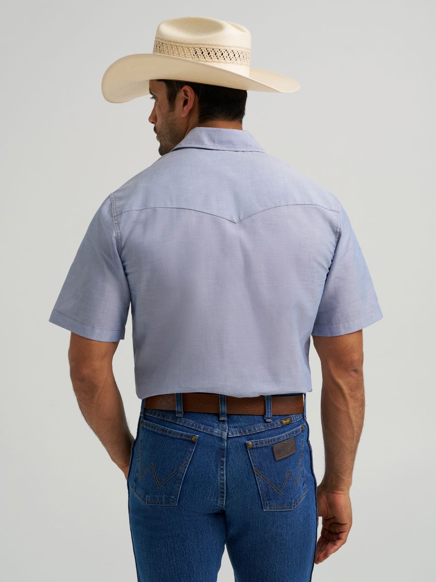 A man wearing a light blue short-sleeve Wrangler western shirt, blue jeans, and a cream cowboy hat, shown from the back against a light gray studio background.