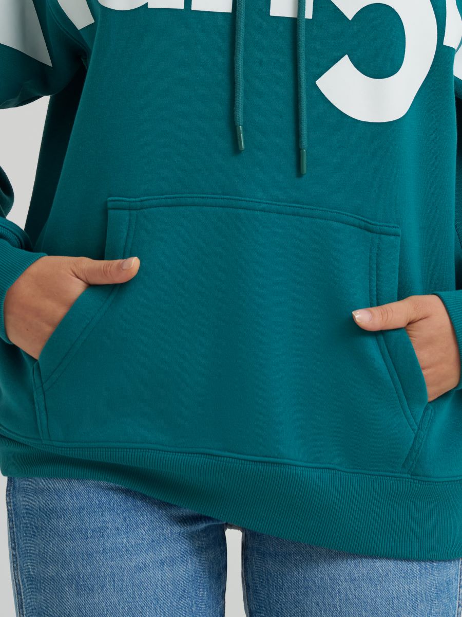 Teal hoodie with white text worn by a person, on a plain background