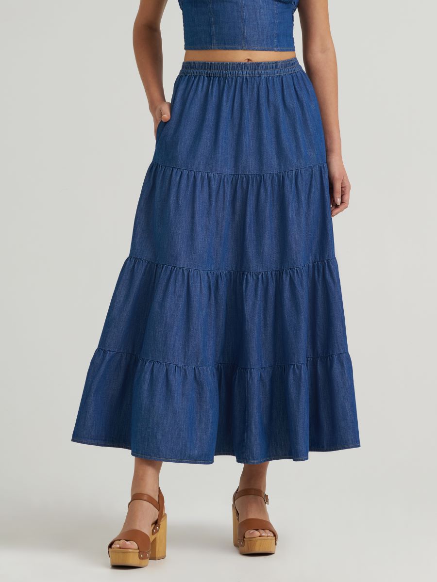 Woman wearing a blue tiered denim skirt on a plain background