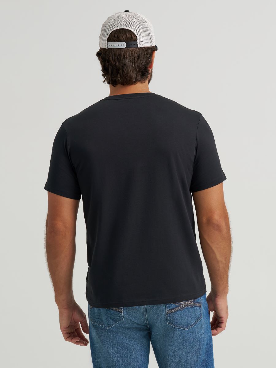 Man wearing a black Wrangler t-shirt and blue jeans with a white cap on a light gray background