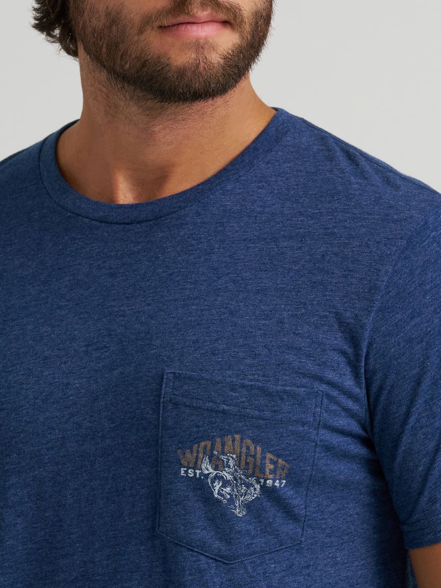 Man wearing a blue Wrangler t-shirt with a logo on the chest pocket against a gray background