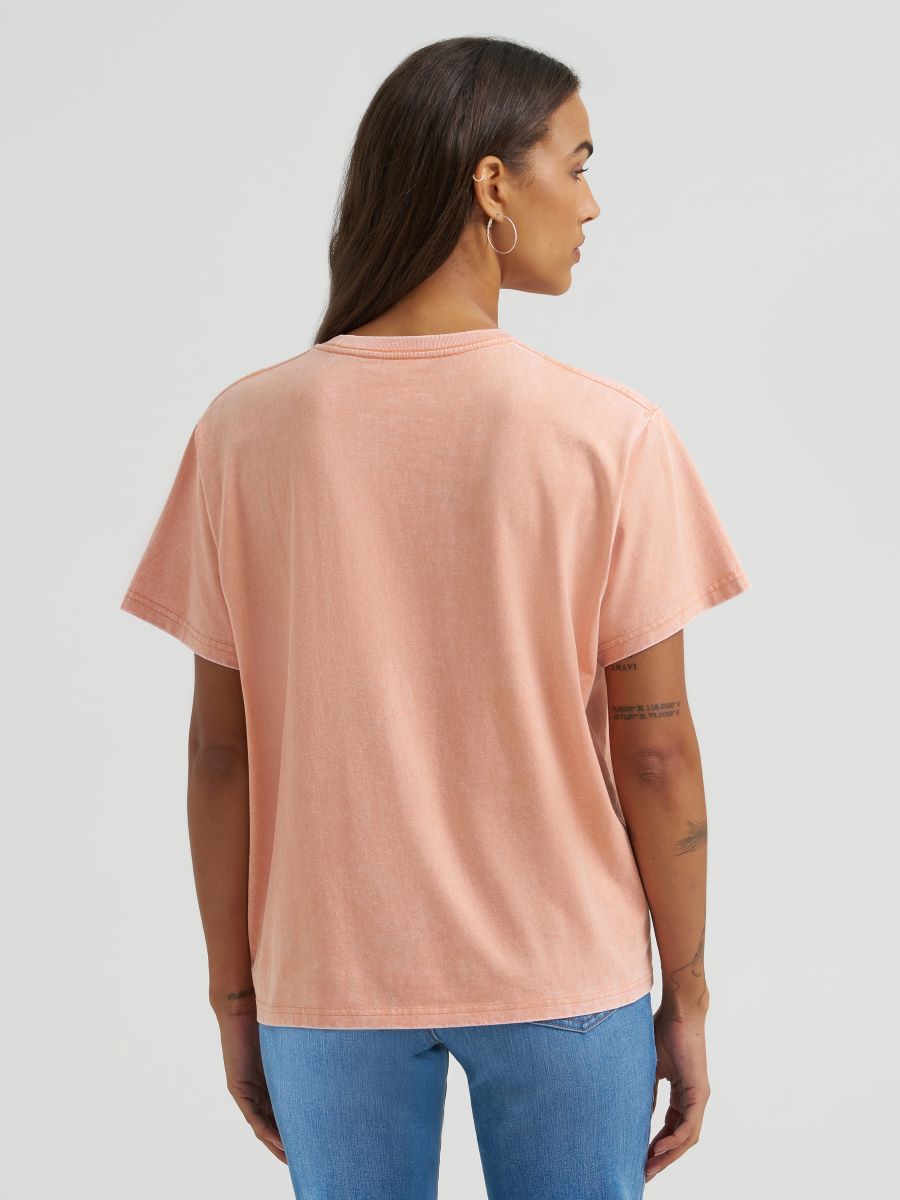Person wearing a light pink Wrangler t-shirt and blue jeans on a plain background
