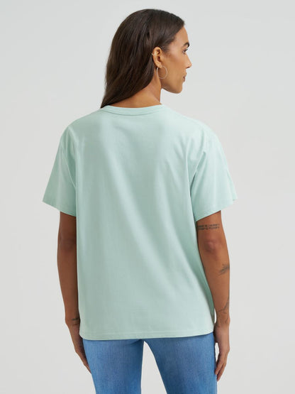 Person wearing a light green Wrangler t-shirt and blue jeans on a plain background