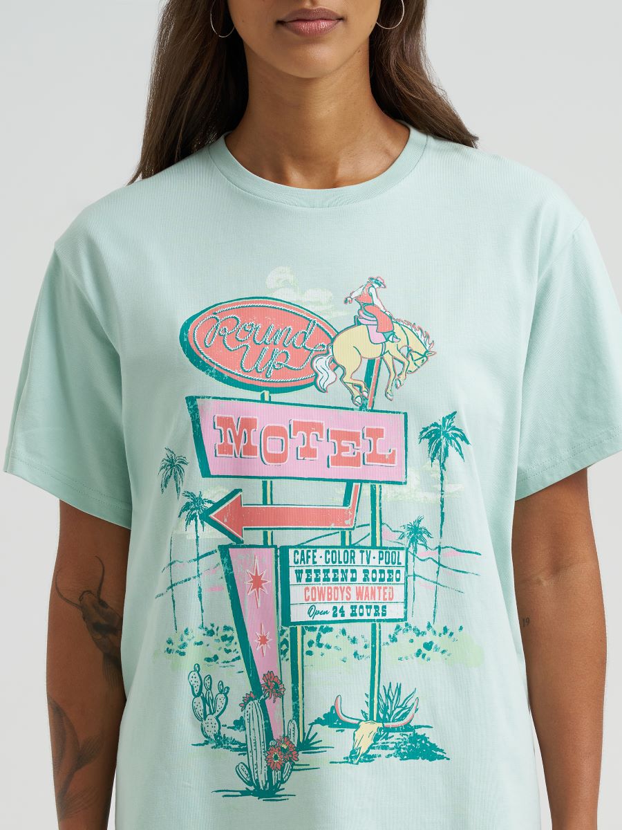 Person wearing a green Wrangler t-shirt with a vintage-style motel sign graphic.