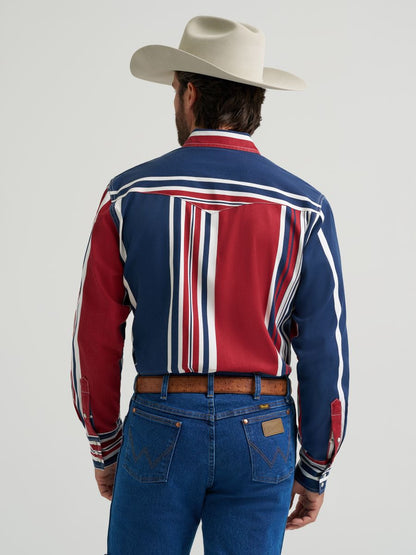 Man wearing a colorful striped Wrangler shirt, blue jeans, and a cowboy hat on a gray background