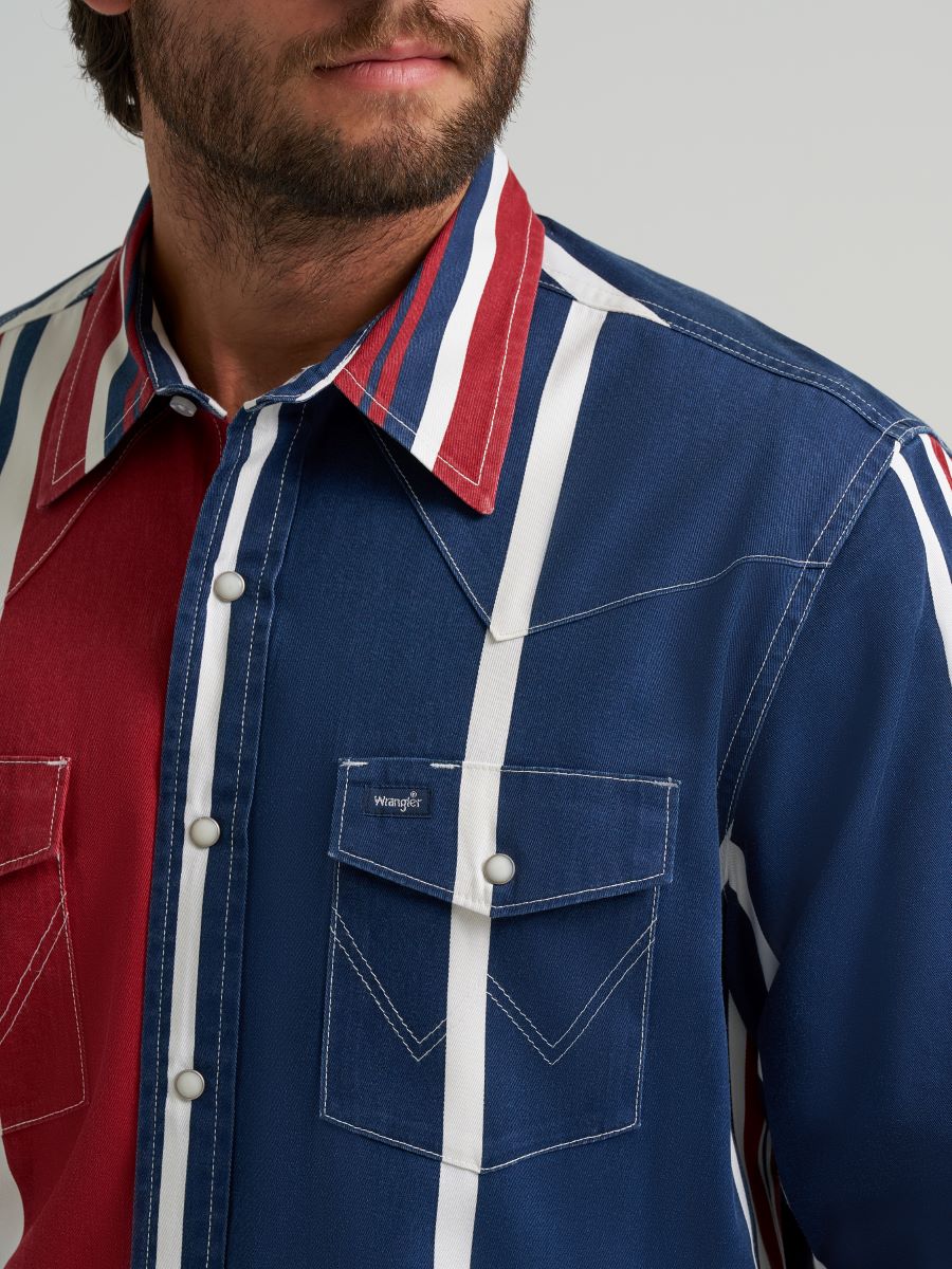 Man wearing a colorful striped Wrangler shirt, blue jeans, and a cowboy hat on a gray background