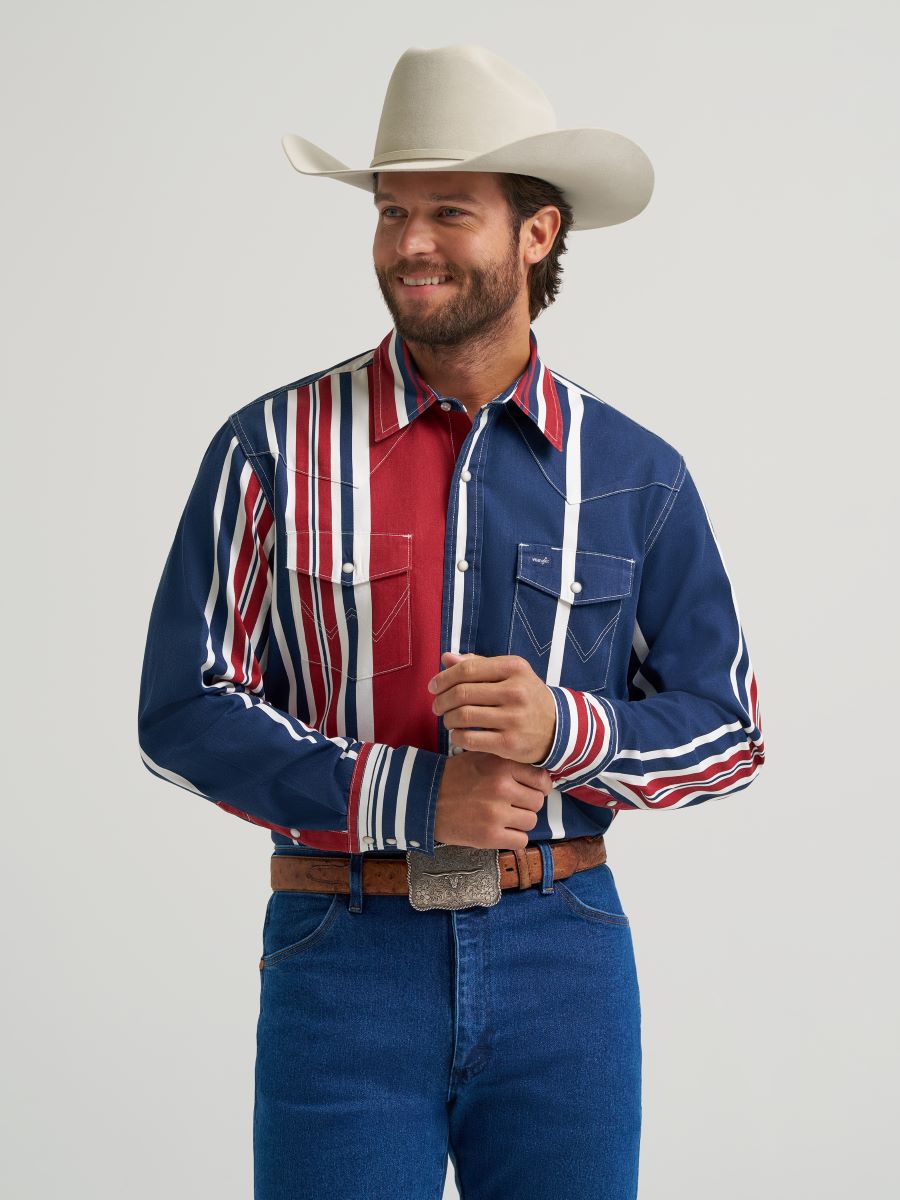 Man wearing a colorful striped Wrangler shirt, blue jeans, and a cowboy hat on a gray background