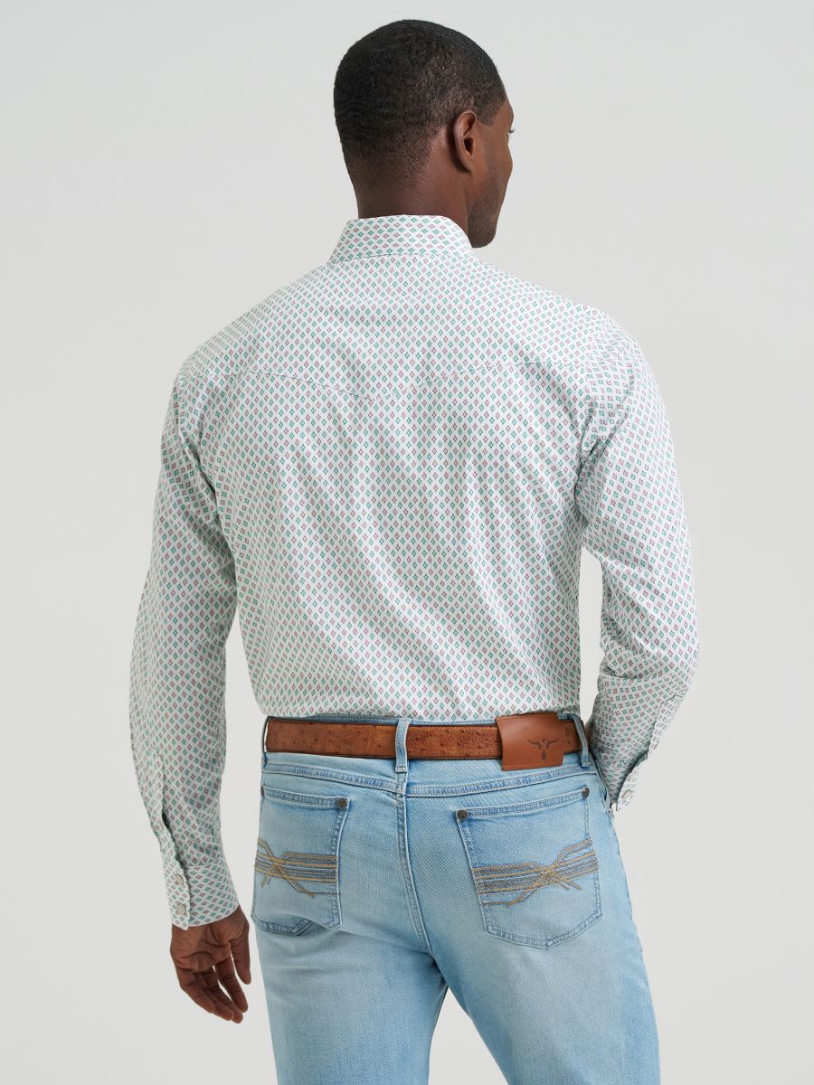 Man wearing a green and brown patterned Wrangler shirt and light blue jeans against a plain background