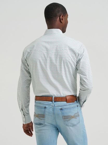 Man wearing a green and brown patterned Wrangler shirt and light blue jeans against a plain background