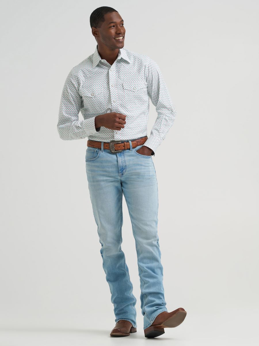 Man wearing a green and brown patterned Wrangler shirt and light blue jeans against a plain background