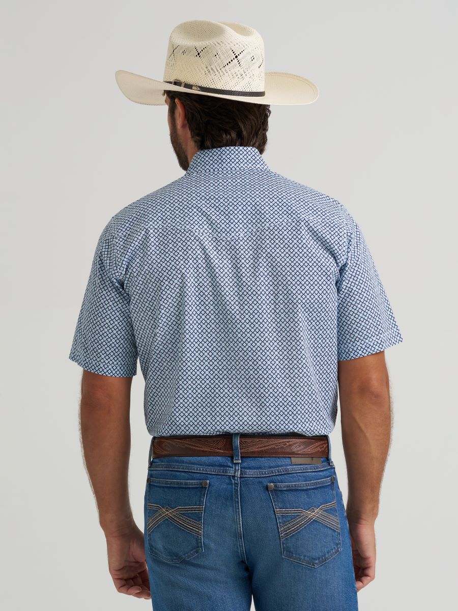 Man wearing a blue patterned Wrangler shirt, white hat, and jeans on a gray background