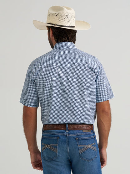 Man wearing a blue patterned Wrangler shirt, white hat, and jeans on a gray background