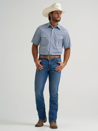 Man wearing a blue patterned Wrangler shirt, blue jeans, and a white cowboy hat on a light gray background