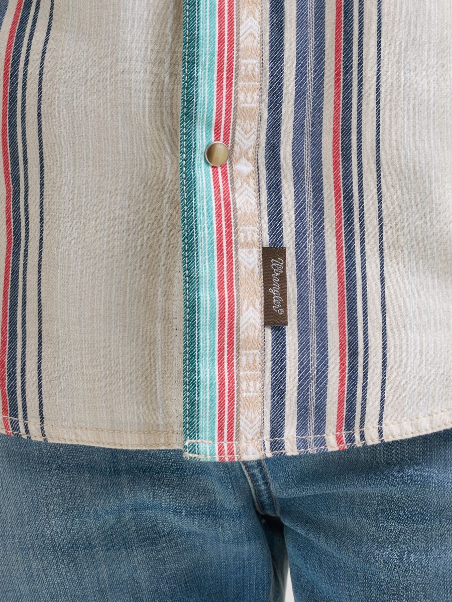 Close-up of a striped shirt with a Wrangler brand label, worn with blue jeans.
